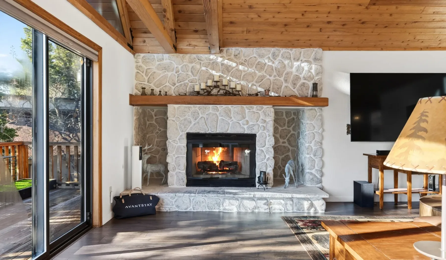 A living room features a stone fireplace beneath a wooden vaulted ceiling.
