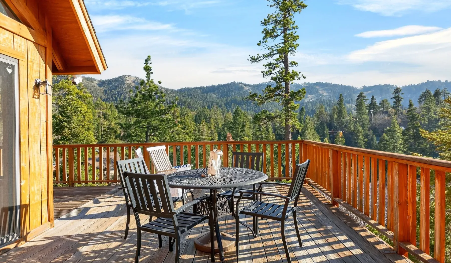 An outdoor deck has a table and seating overlooking a forested mountain landscape.