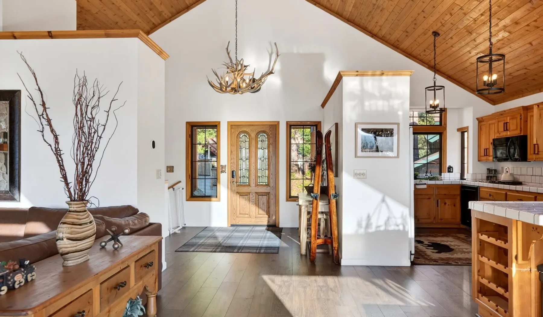 A vaulted living room opens into a kitchen, with wood cabinetry and a high timber ceiling.