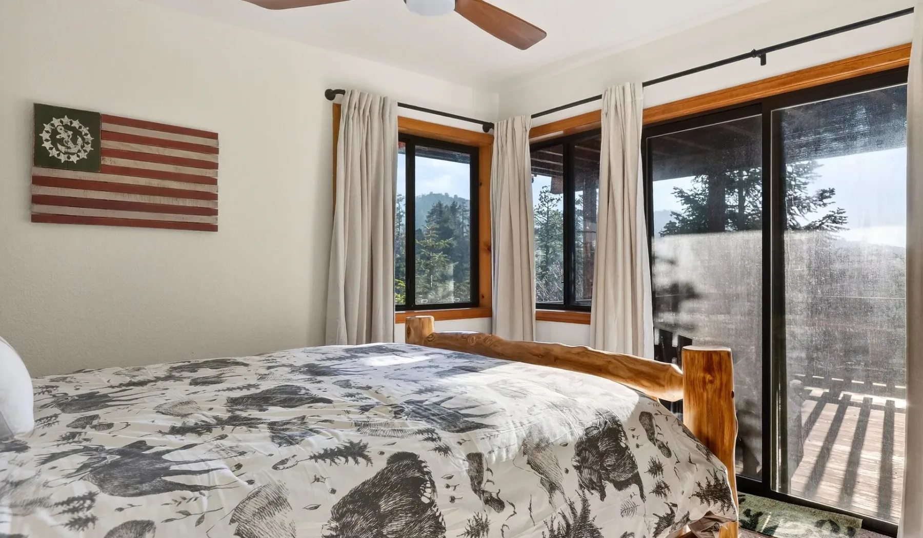A bedroom with patterned bedding, curtained windows, and a sliding glass door.