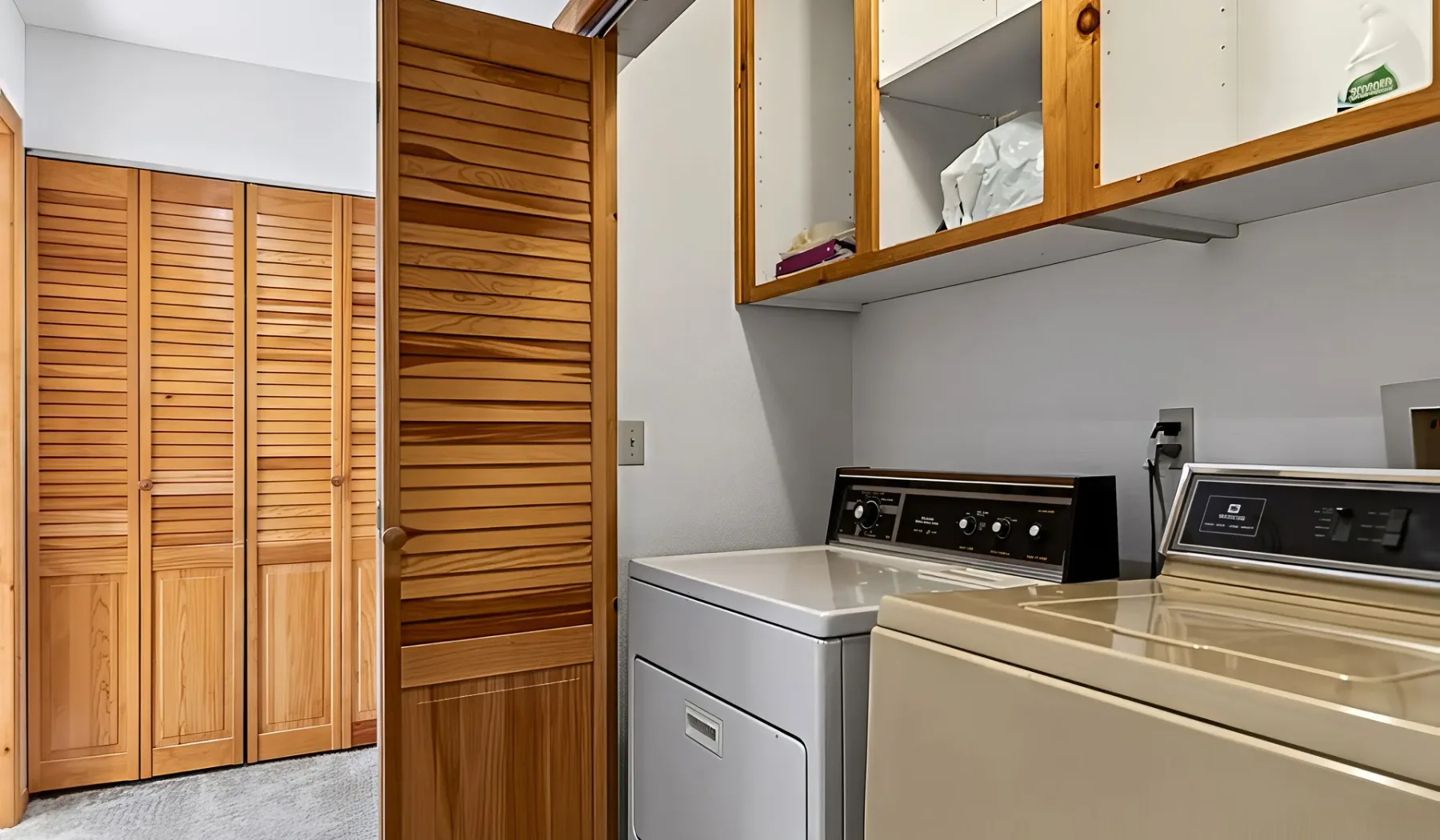 A laundry room with a washer, dryer, and overhead storage cabinets.