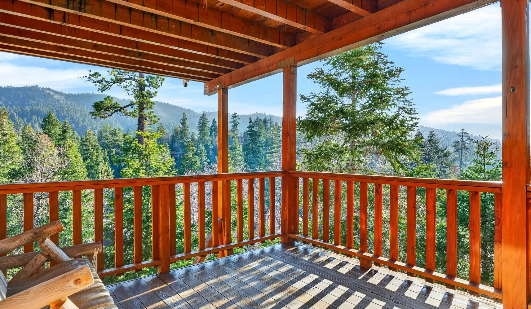 A covered wooden deck overlooks a forested mountain landscape.