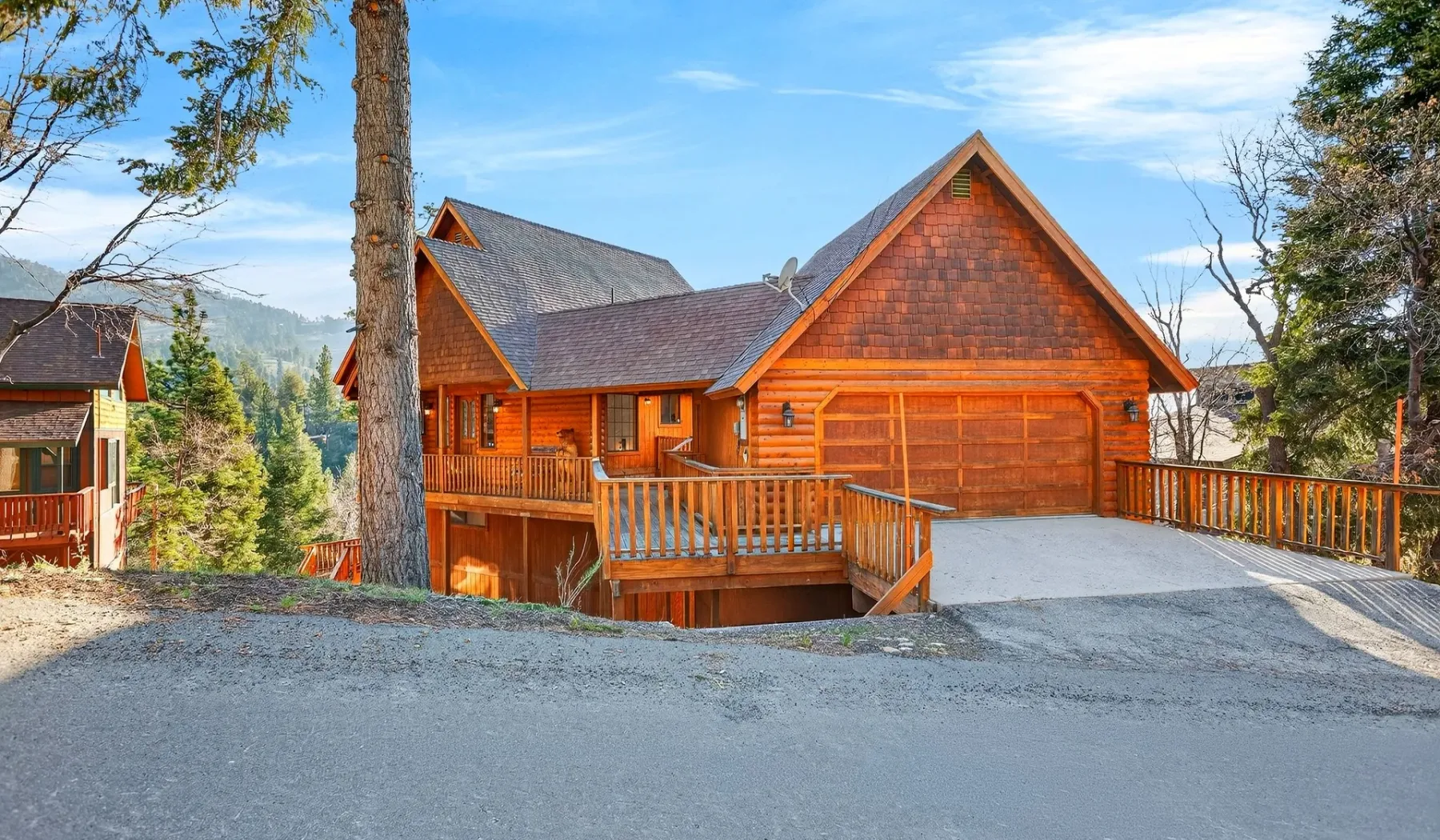 A wooden cabin with a broad driveway and surrounding trees.