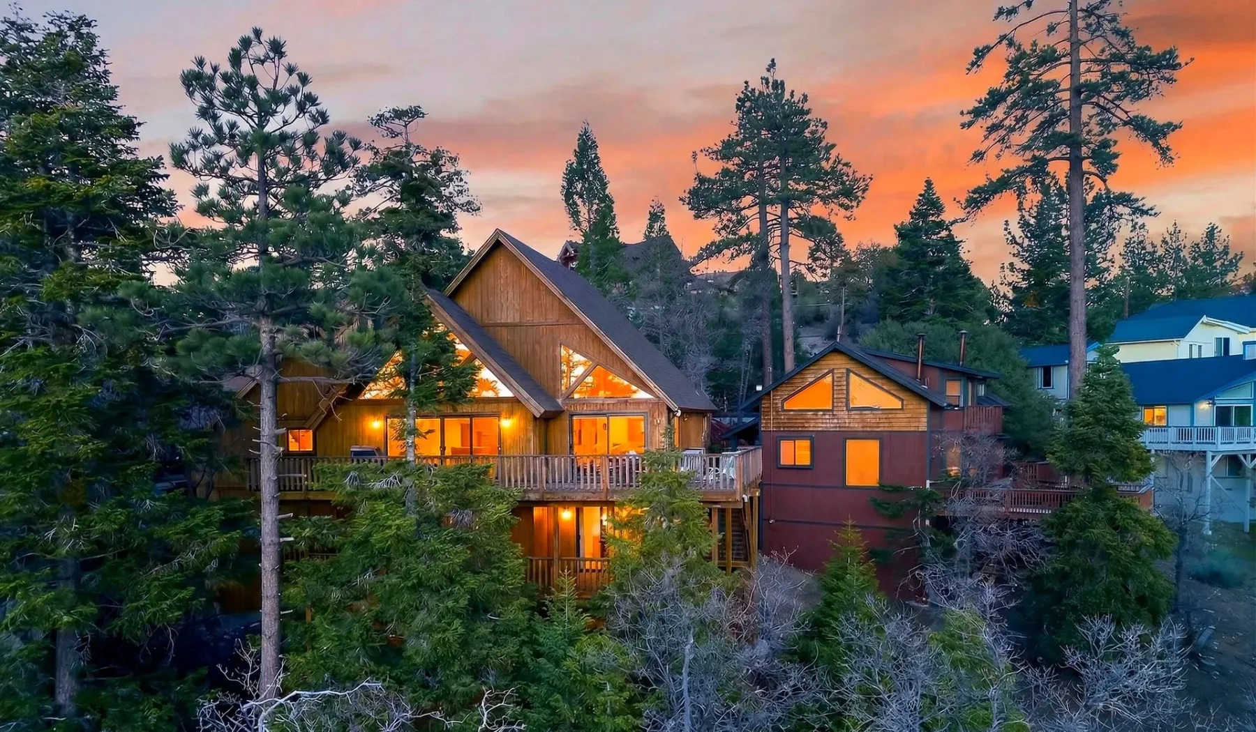 Woodland cabins glow beneath a colorful sunset sky.