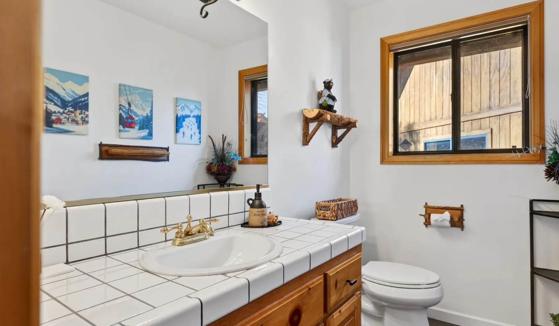 A bathroom with a tiled vanity and toilet beneath a wood-framed window.