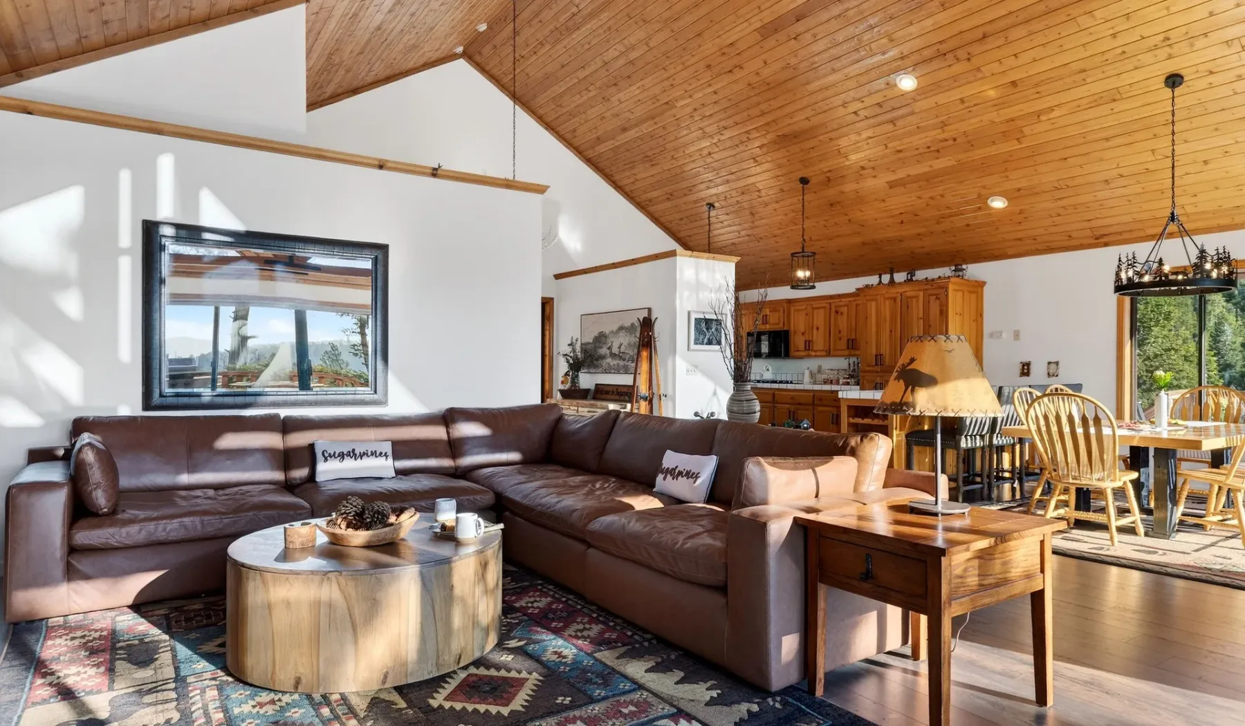 A living room with sectional seating and an open kitchen beneath a wood-paneled ceiling.