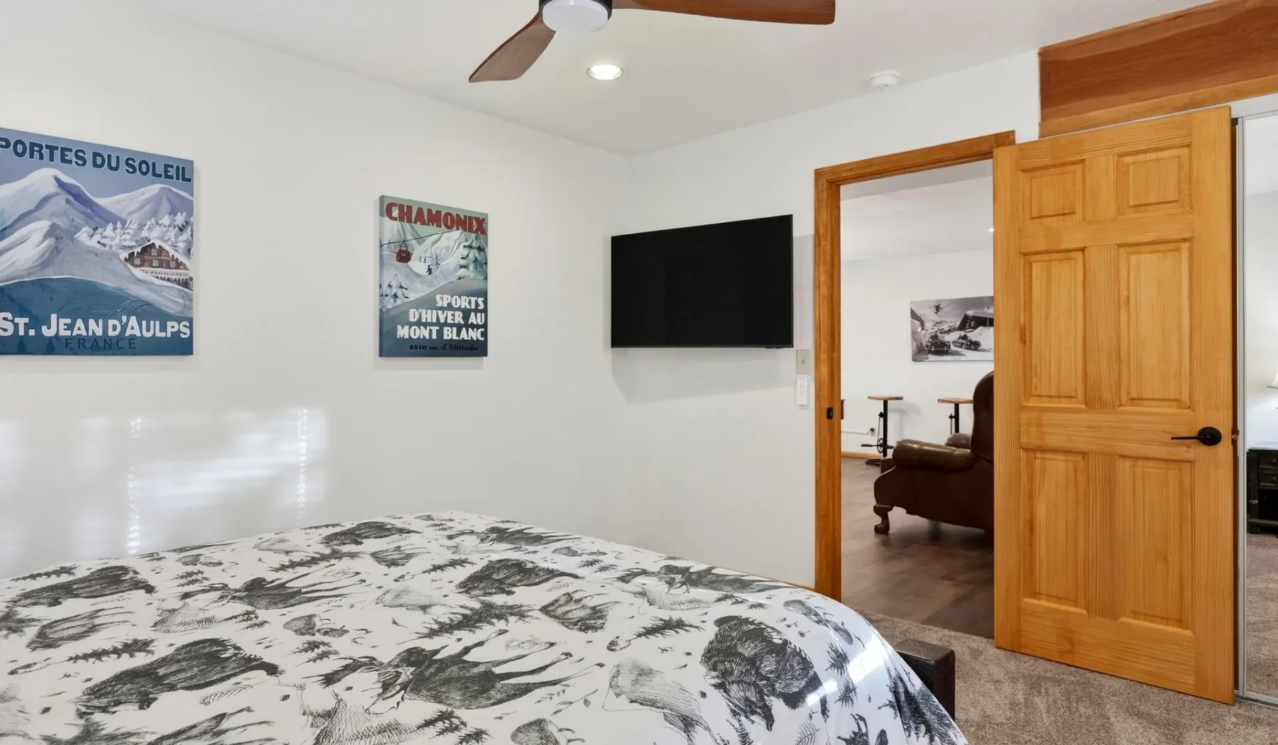 A bedroom with a patterned bedspread, wall-mounted television, and an open wooden door.