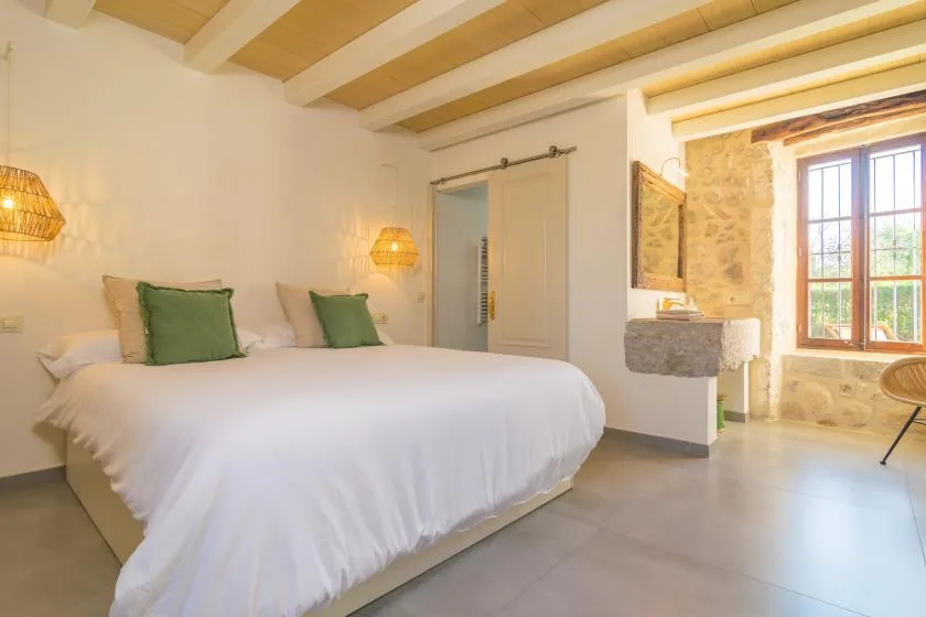 A bedroom with a large bed, exposed ceiling beams, and a window.