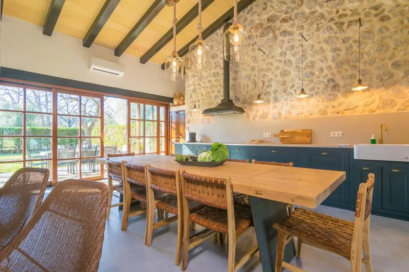 A spacious kitchen and dining area with a long wooden table and stone wall.