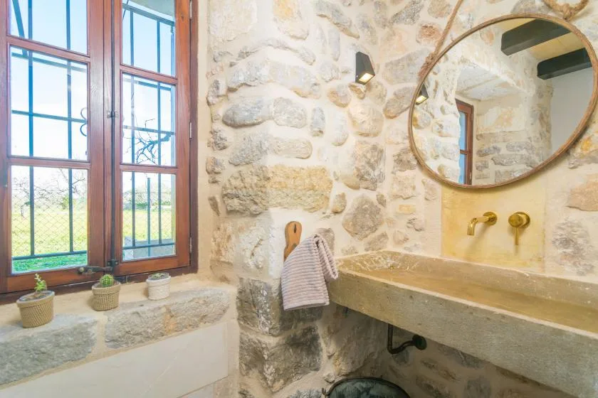A rustic bathroom with a stone wall, wide sink, and round mirror.