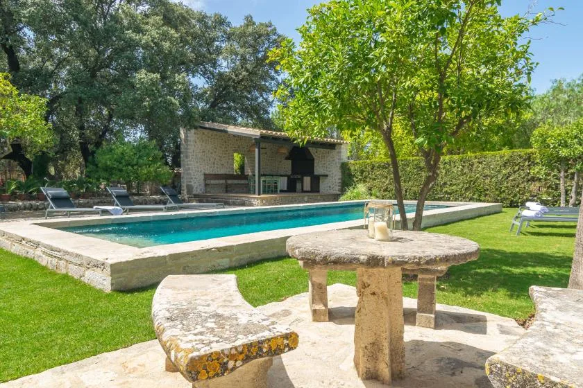 An outdoor pool beside a stone patio table, seating, and a shaded garden pavilion.