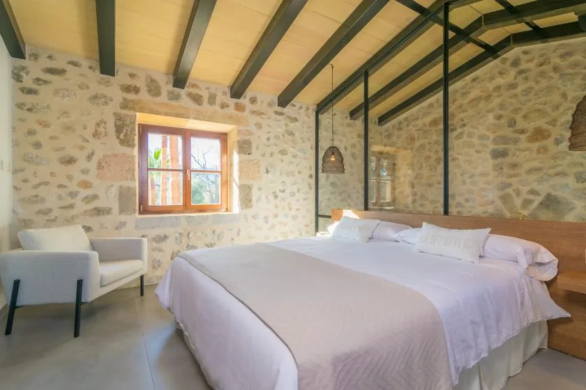 A bedroom with a bed, a window, and a stone wall.