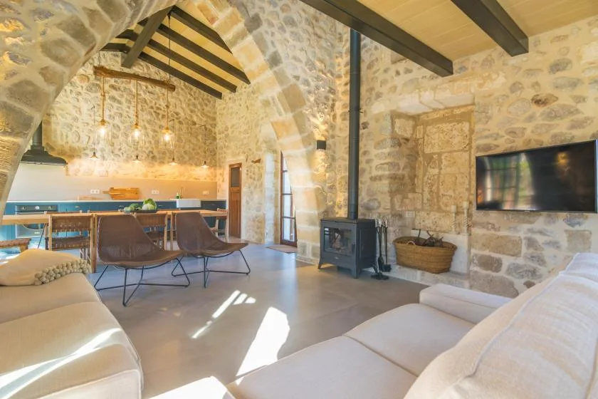 A stone-walled living room with seating, a television, and an adjoining dining area.
