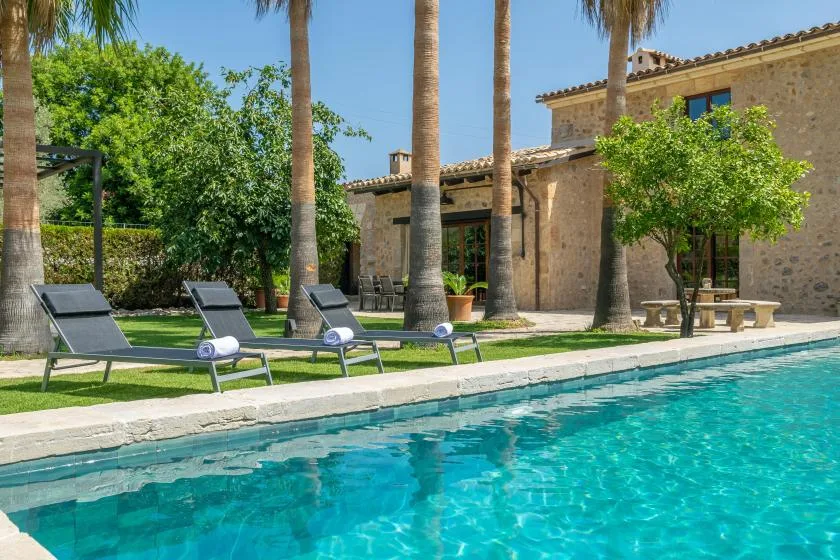 A swimming pool beside a stone building, with lounge seating along the edge.