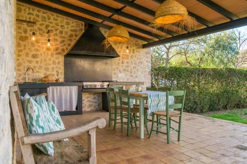 A covered outdoor dining area with a stone cooking counter and wooden table.