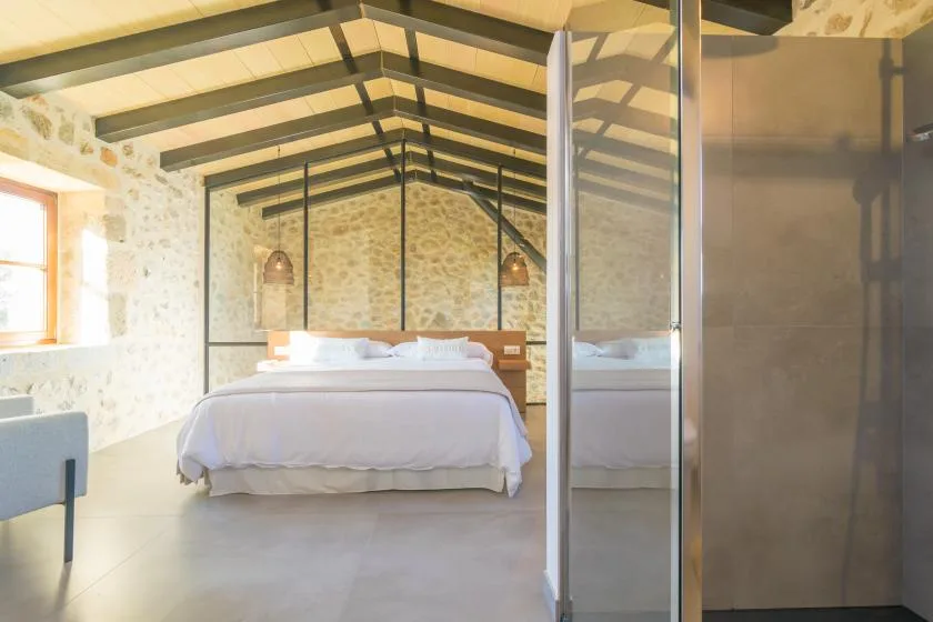 A bedroom with a neatly made bed beneath exposed roof beams.