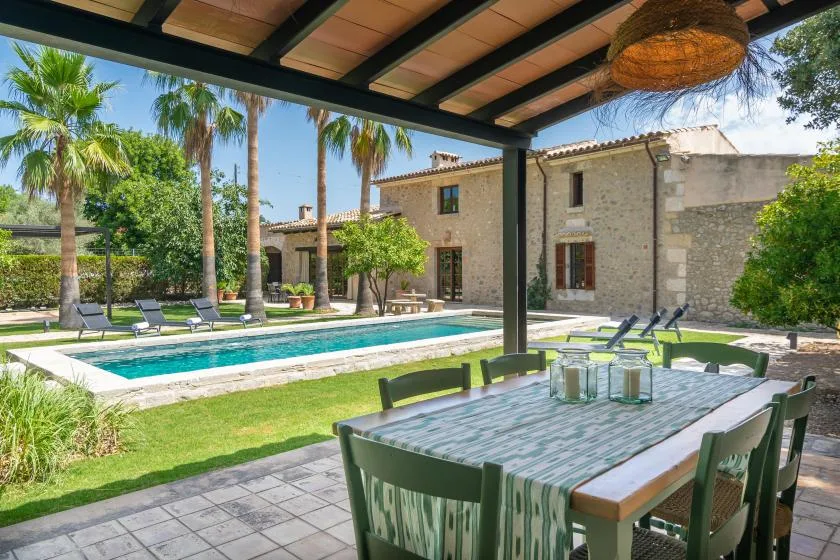 A covered patio dining area overlooks a swimming pool and landscaped garden.
