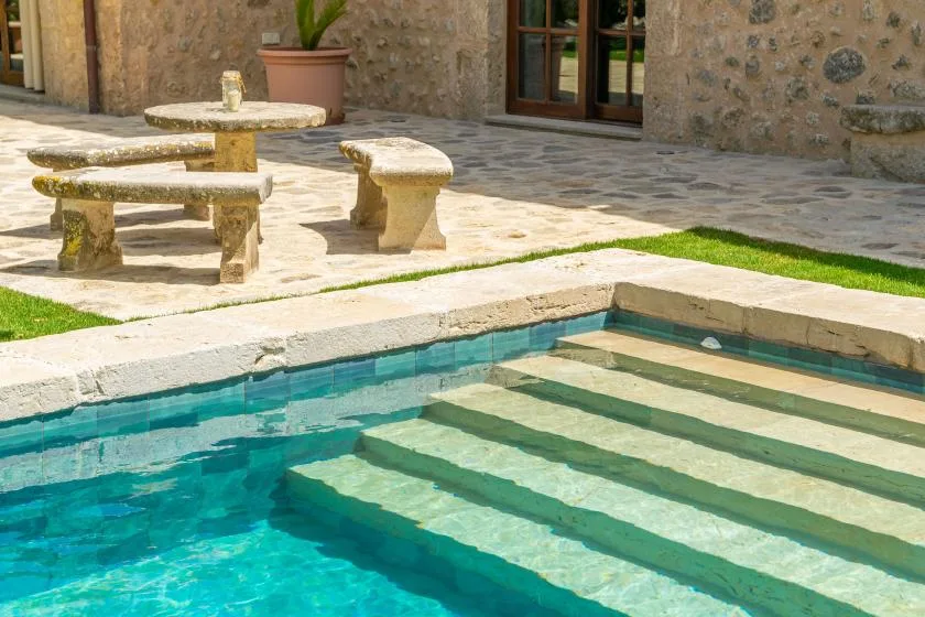 A swimming pool with broad submerged steps beside a stone patio.
