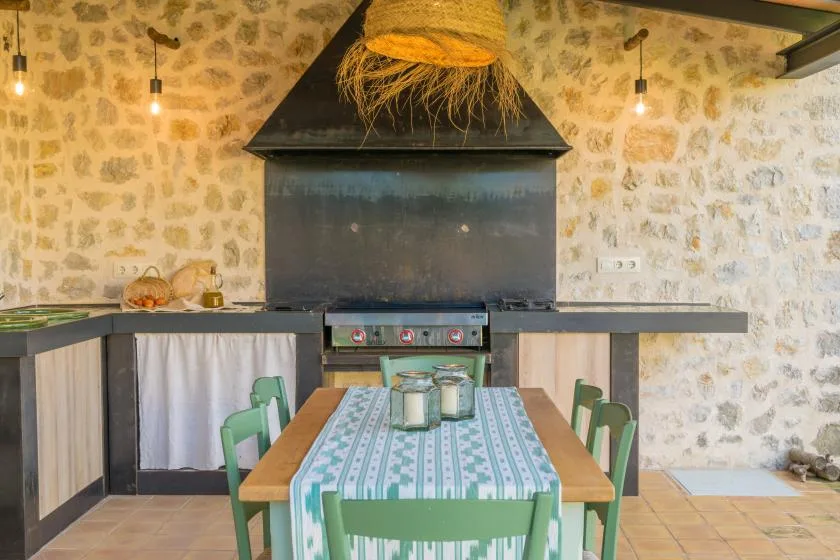 A dining table sits in front of a large built-in grill in a stone-walled room.
