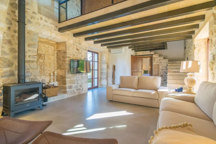 A stone living room with beige seating, exposed beams, and a fireplace.