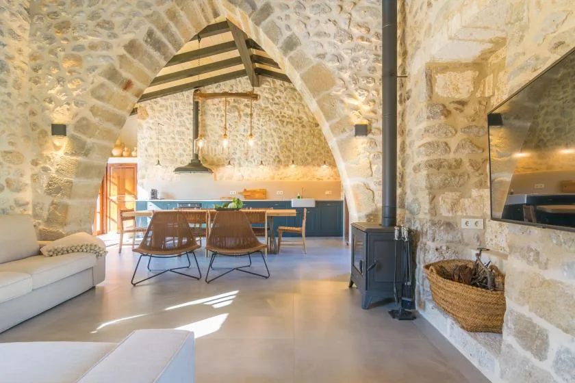 A stone-walled living and dining area opens onto a kitchen beneath an arched ceiling.