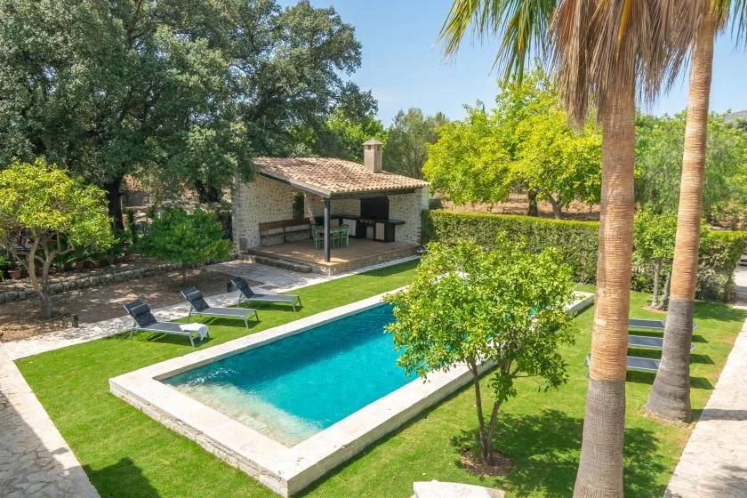 A swimming pool and covered patio sit among green lawns and trees.