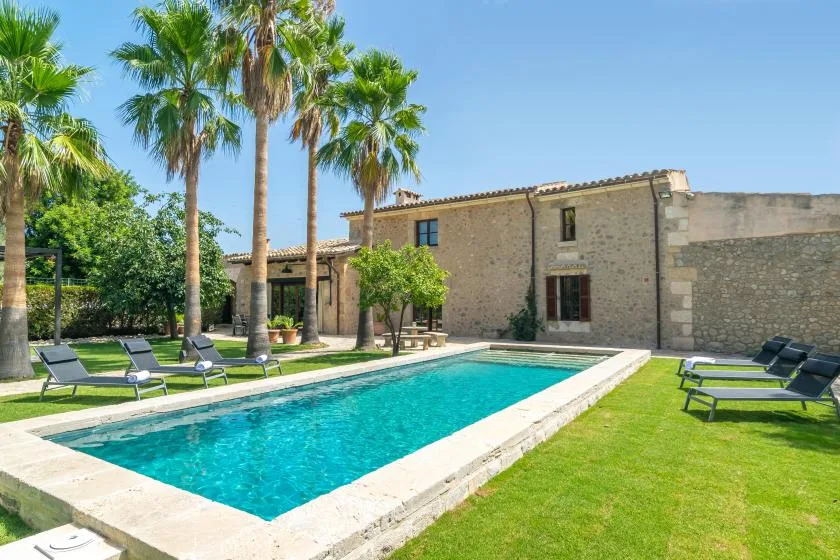 A swimming pool beside a stone building, with lounge seating on the lawn.
