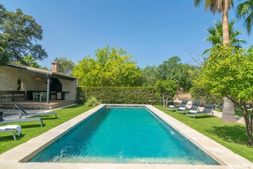 Una piscina al aire libre está junto a un césped y una zona de estar cubierta.