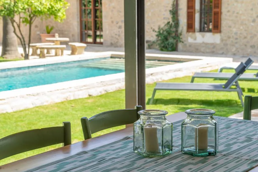 A sunny outdoor patio overlooks a swimming pool, with a table and loungers.