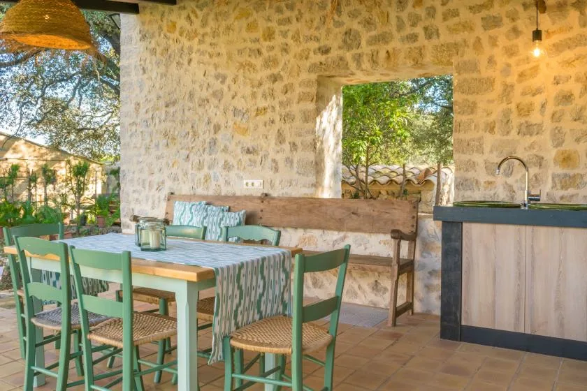 An outdoor dining area with a long table and green seating beside a stone wall.