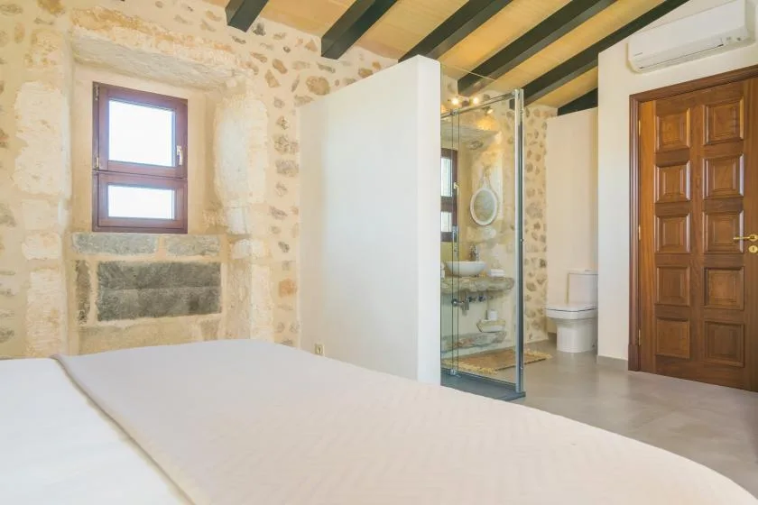 A bedroom with a bed and an adjoining bathroom with a glass shower.