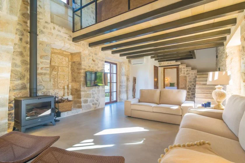 A bright living room with seating, a fireplace, and exposed ceiling beams.