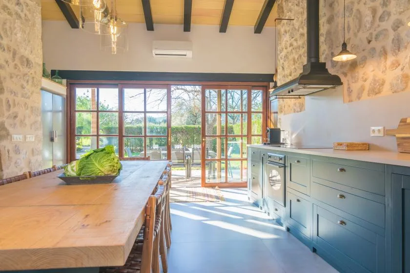 A bright kitchen with a long wooden table and large glass doors.