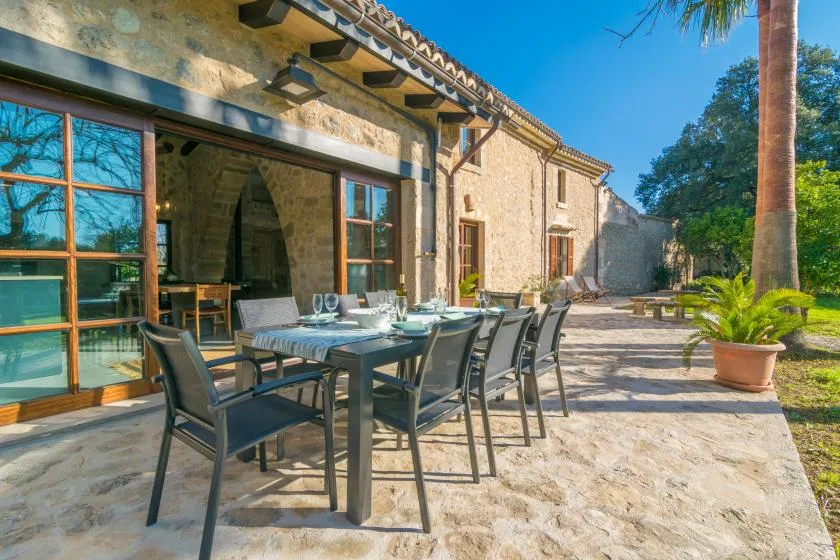 A stone patio with an outdoor dining table and seating beside a house.
