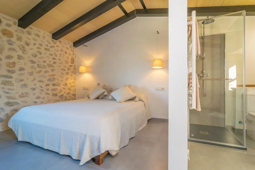 A bedroom with a bed beside a glass-enclosed shower.