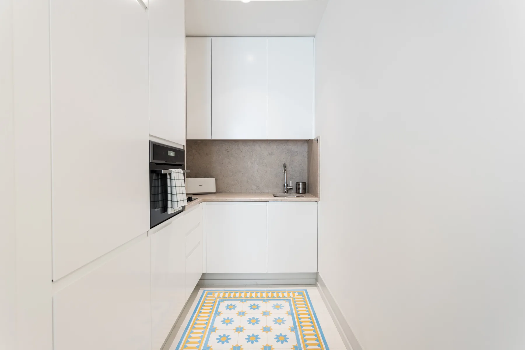 A bright white kitchen with built-in appliances and a patterned floor runner.
