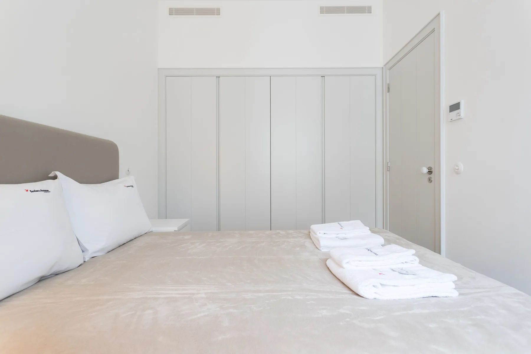 A bright bedroom with a bed and neatly folded white towels.