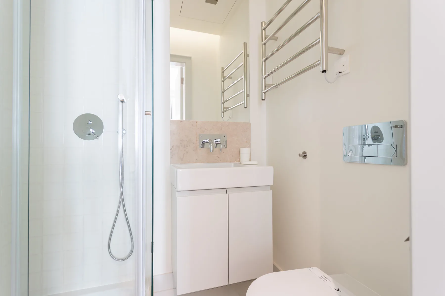 Un baño con ducha, lavabo y toalleros montados en la pared.