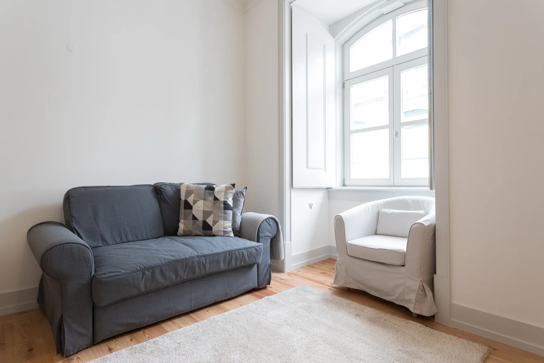 Una sala luminosa con un sofá gris y una ventana grande.
