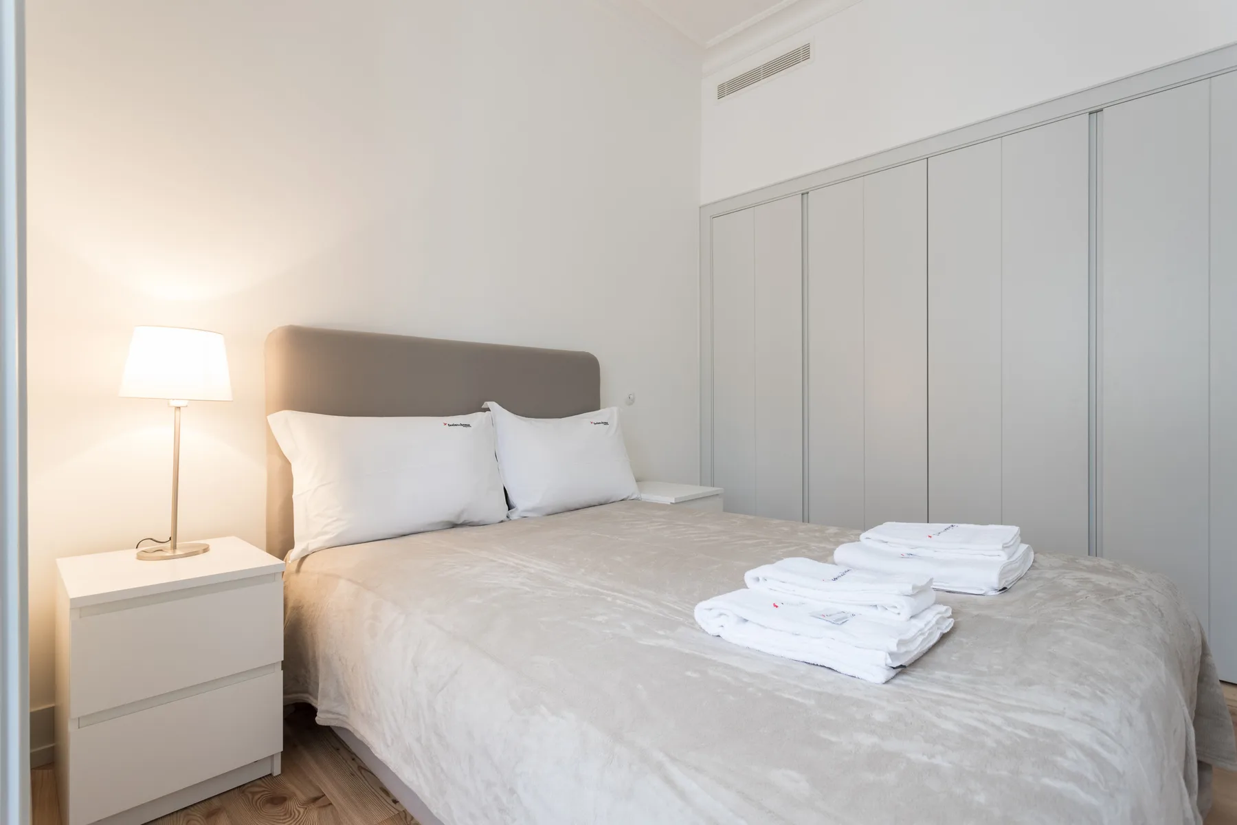 A bedroom with a neatly made bed and folded towels.