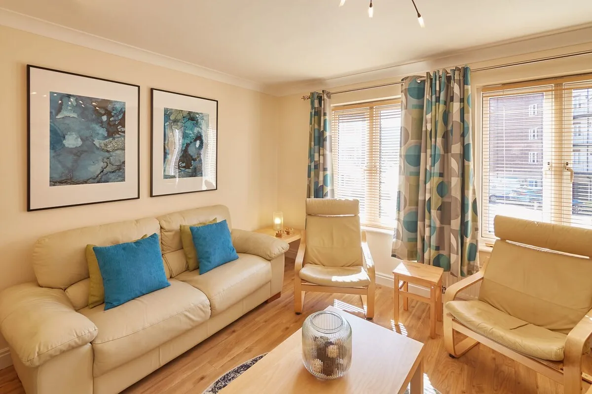 A bright living room with seating, framed artwork, and large windows.