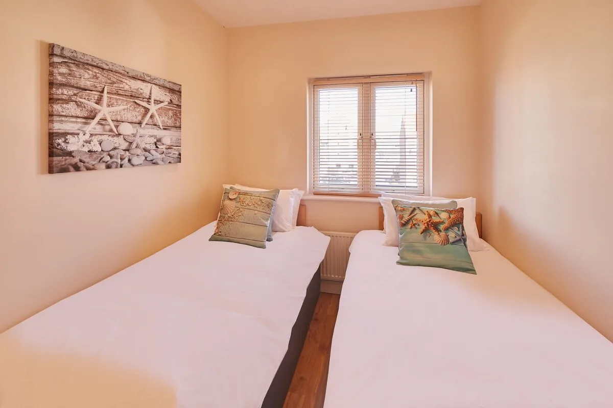 A bedroom with two beds beneath a window with blinds.