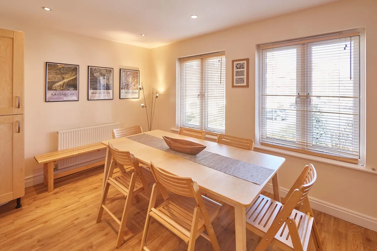 A dining room with a long table and wooden seating beside large windows.