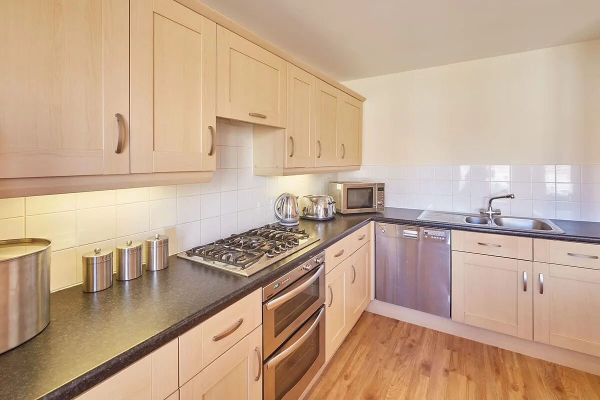 A kitchen with pale cabinets, a cooktop, and a sink along the counter.