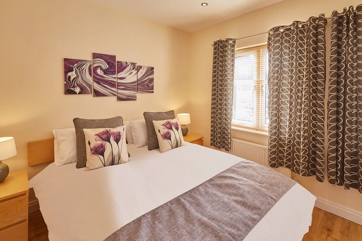 A bedroom with a bed, patterned pillows, and curtains beside the window.