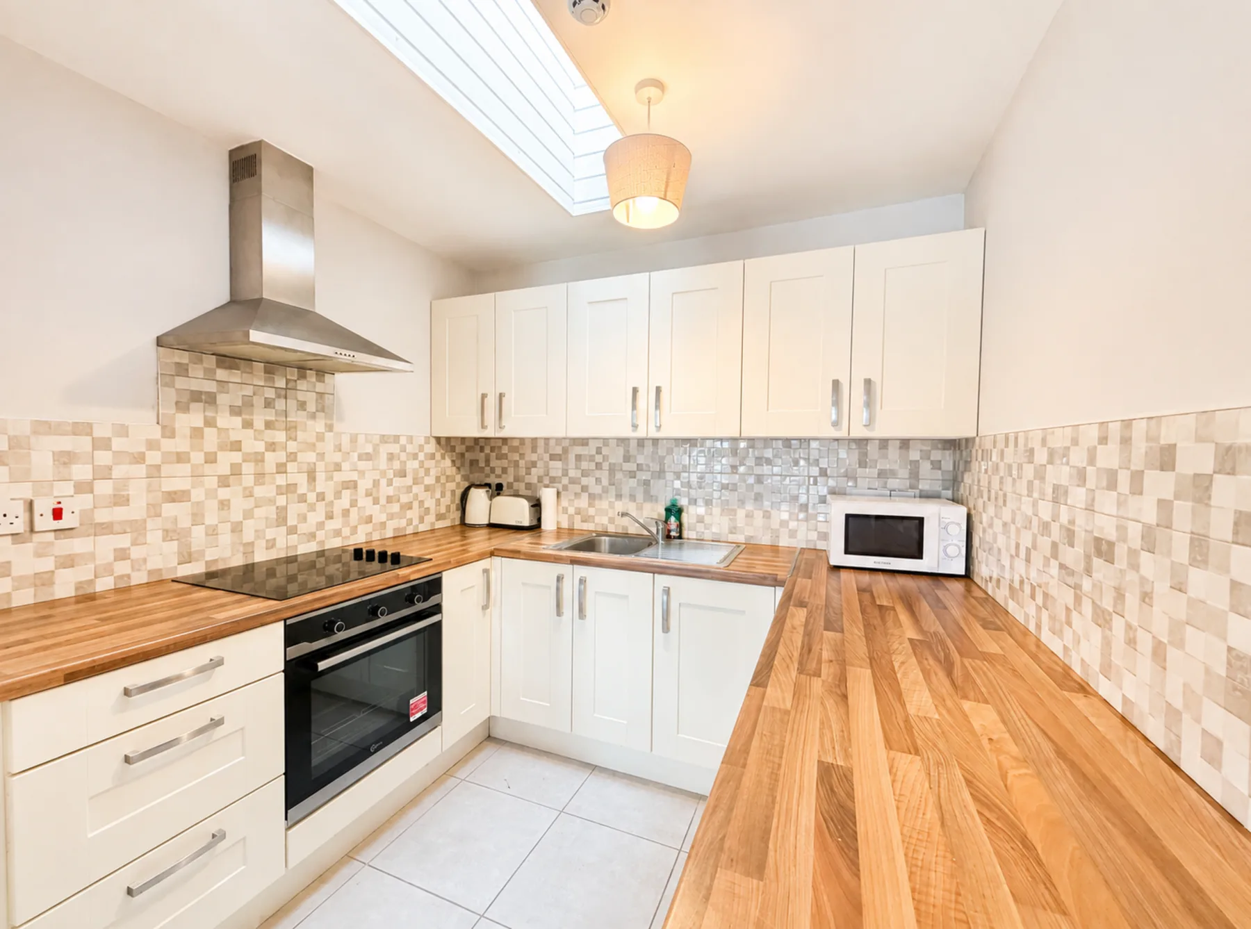 Una cocina luminosa con gabinetes blancos, salpicadero de azulejos y encimeras de madera.