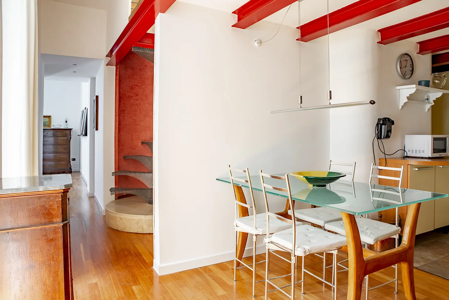 A dining area with a glass table and white chairs beneath red ceiling beams.