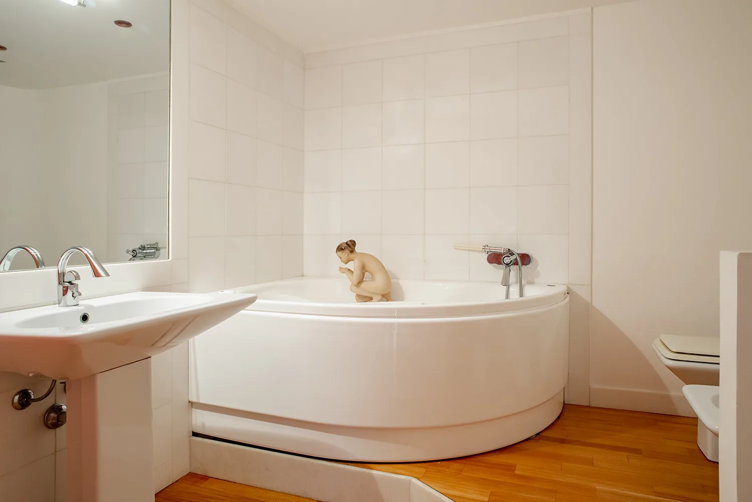 A tiled bathroom with a curved bathtub, sink, and wooden floor.