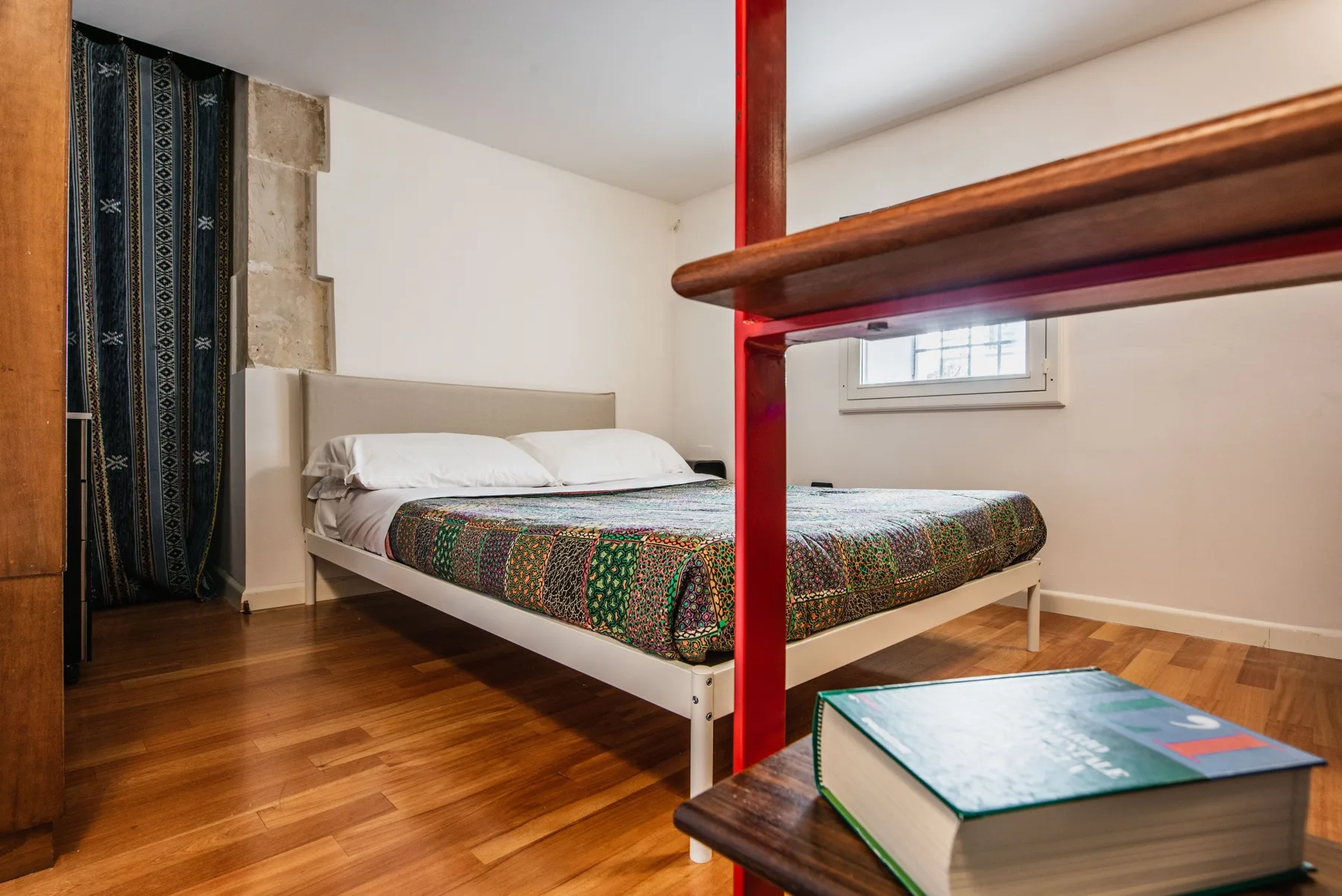 A bedroom with a bed, patterned cover, and a small window.