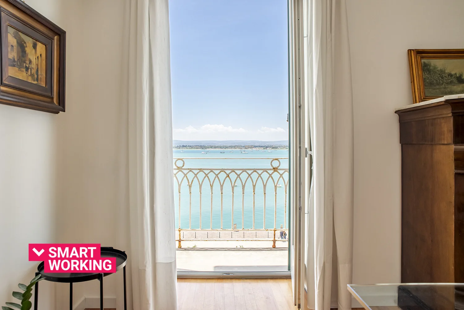 A bright room opens onto a balcony with views of the sea.